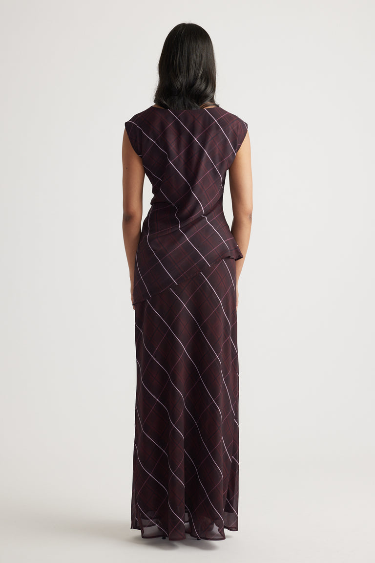 Woman seen from behind wearing a sleeveless dark checkered maxi dress with subtle diagonal lines against a plain background