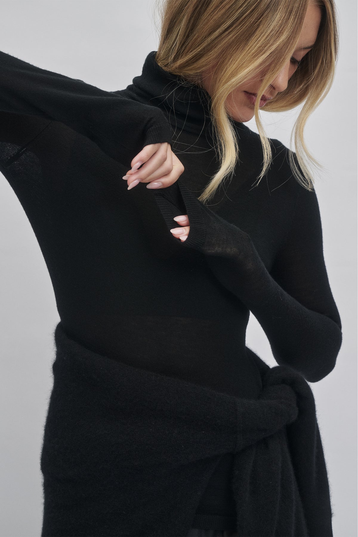 Close-up of a woman wearing a soft black fine wool knit top with thumb holes, styled with a cozy knit wrap around her waist.