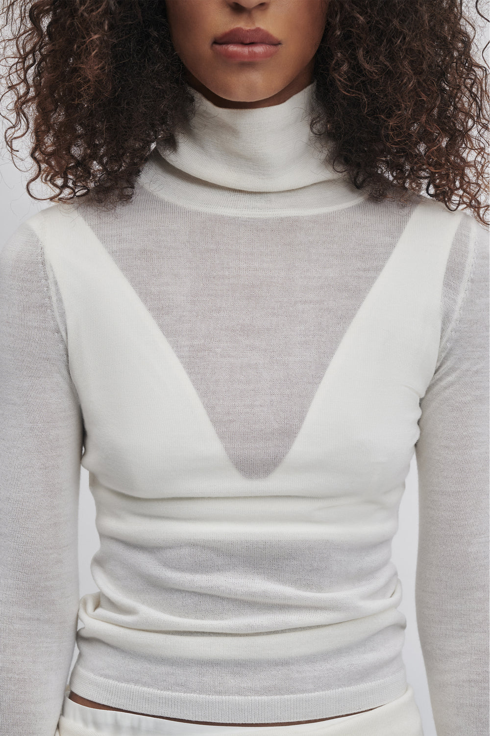 Close-up of woman wearing a soft ivory fine wool knit top with a high neck and layered sheer details.