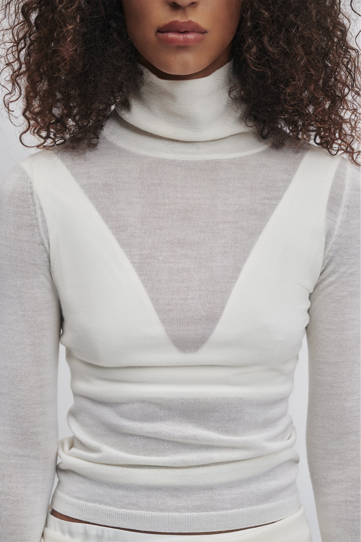 Close-up of woman wearing a soft ivory fine wool knit top with a high neck and layered sheer details.