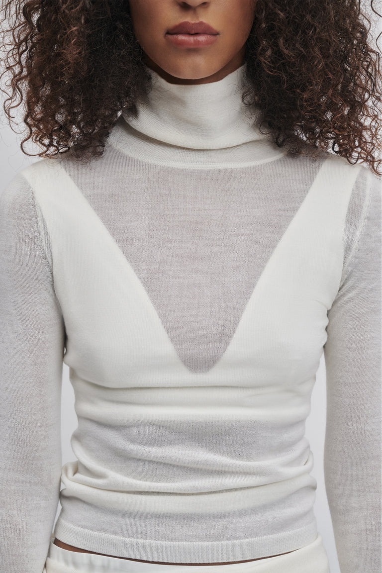 Close-up of woman wearing a soft ivory fine wool knit top with a high neck and layered sheer details.