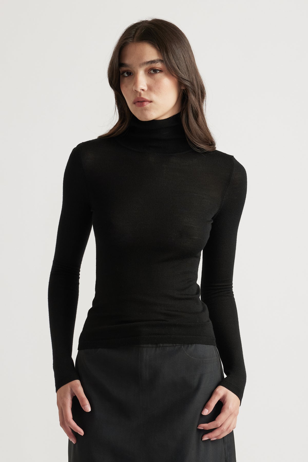 Woman wearing a sleek black fine wool knit top with a high neckline paired with a dark skirt for a polished look