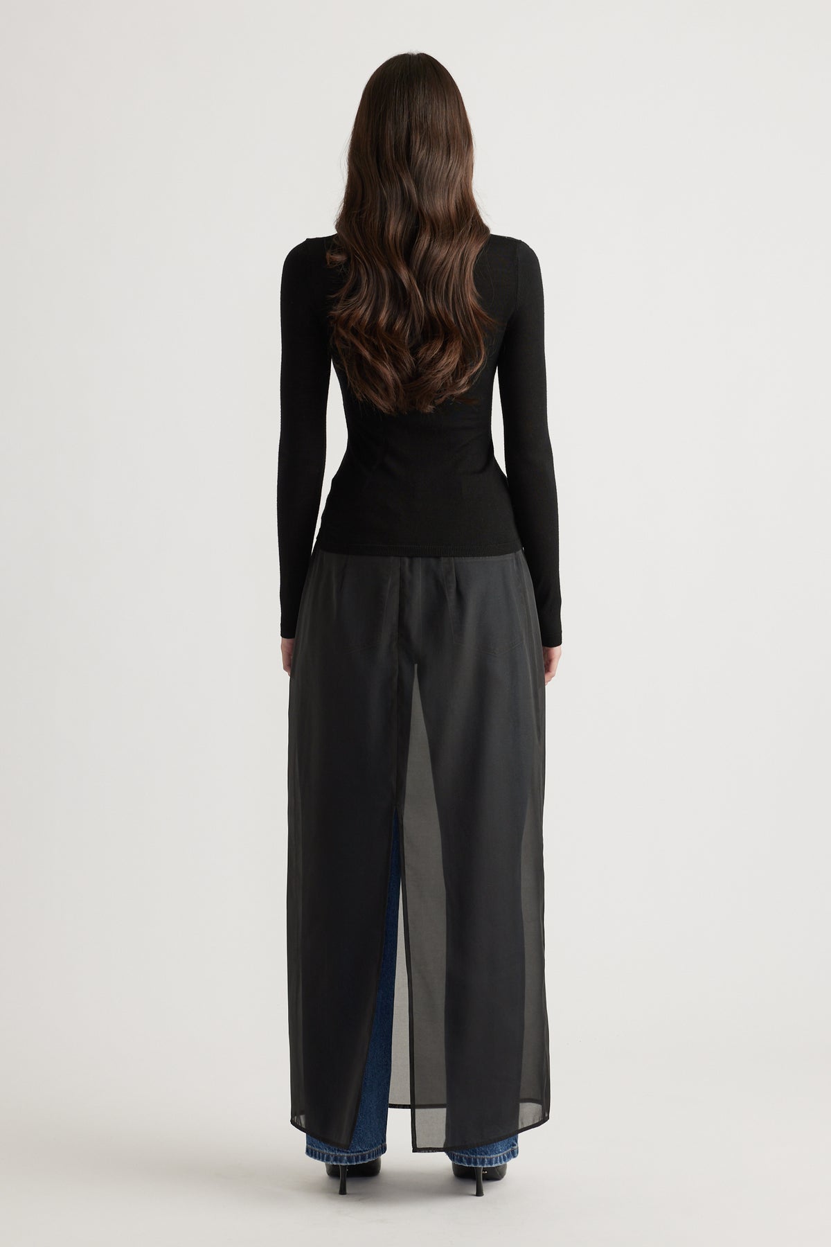 Back view of woman wearing a fitted black fine wool knit top paired with layered wide-leg pants and heels