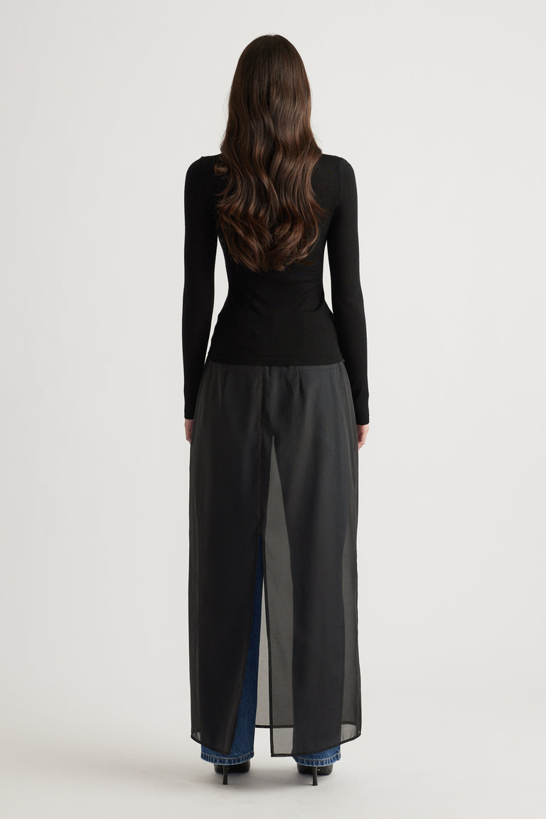 Back view of woman wearing a fitted black fine wool knit top paired with layered wide-leg pants and heels