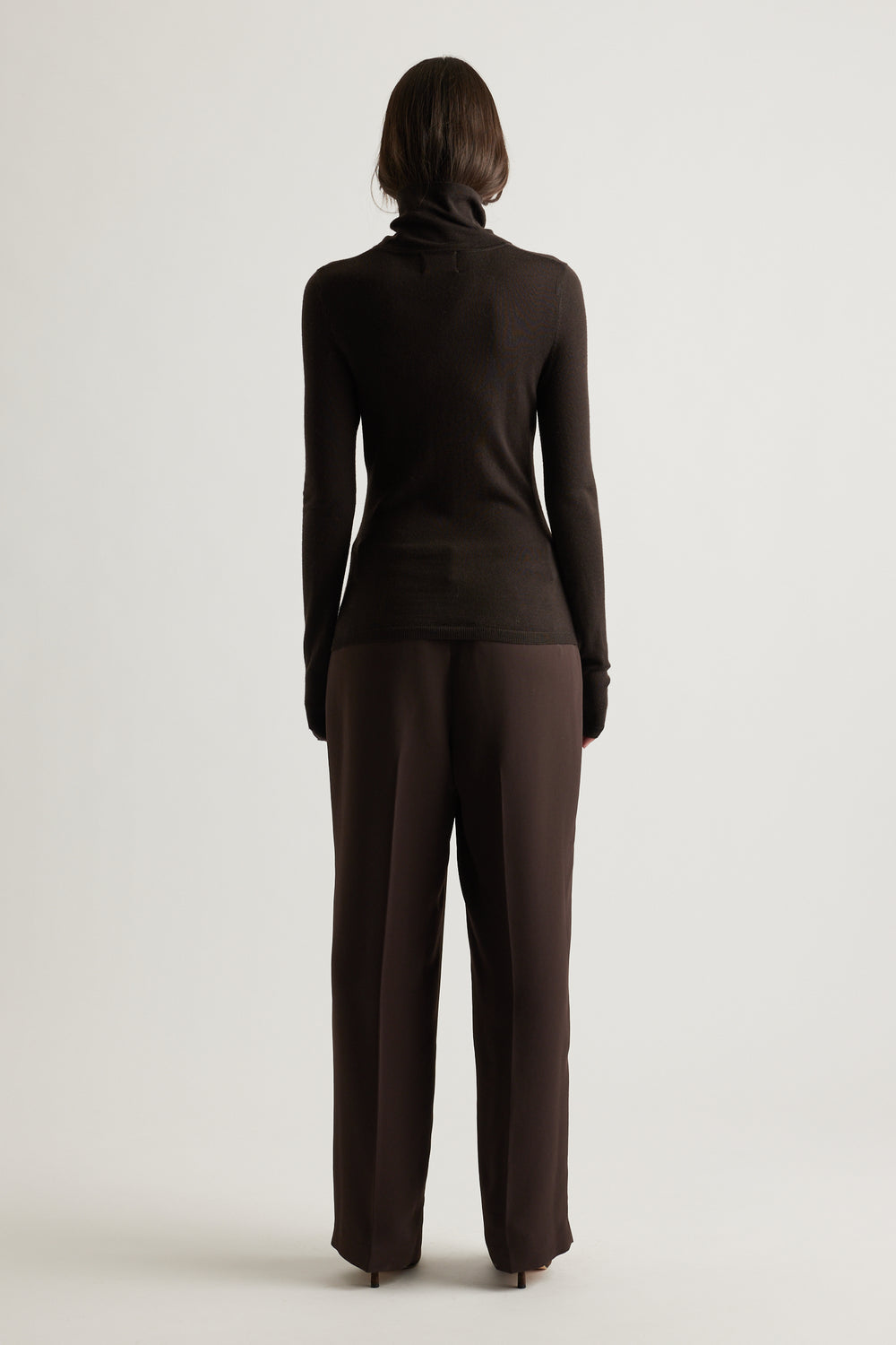 Rear view of woman wearing a fitted dark brown fine wool knit top paired with loose, matching trousers for a sleek look