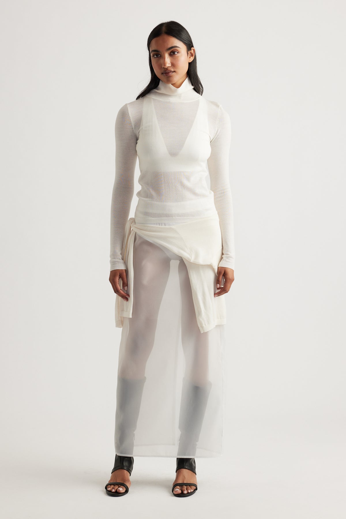 Woman wearing a layered ivory knit top dress with sheer fabric and black open-toe heels for a minimalist look