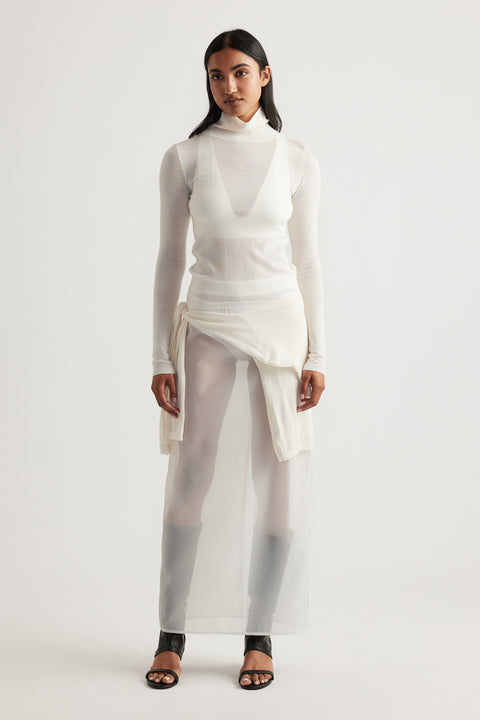 Woman wearing a layered ivory knit top dress with sheer fabric and black open-toe heels for a minimalist look