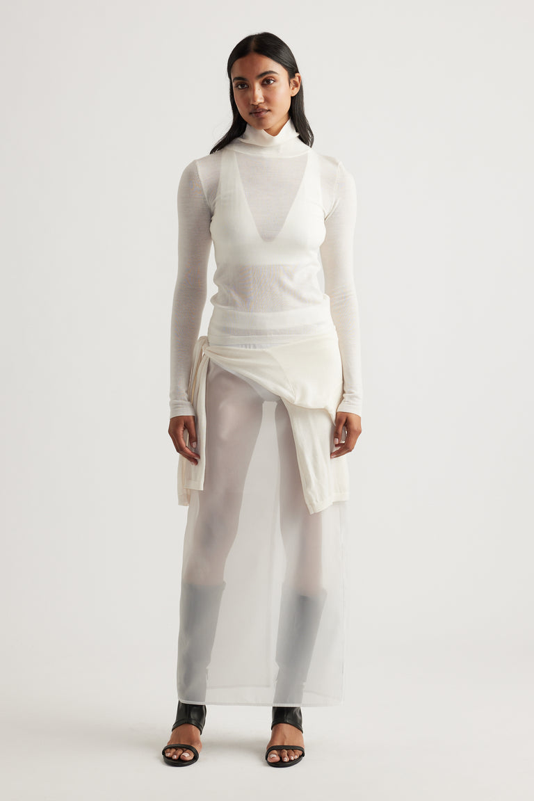Woman wearing a layered ivory knit top dress with sheer fabric and black open-toe heels for a minimalist look