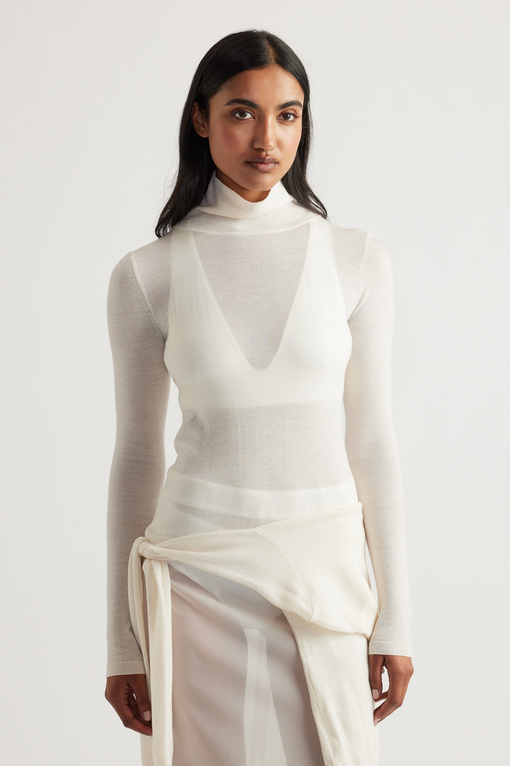 Woman wearing a sheer ivory knit top layered over a sleeveless knit vest with a soft draped skirt detail