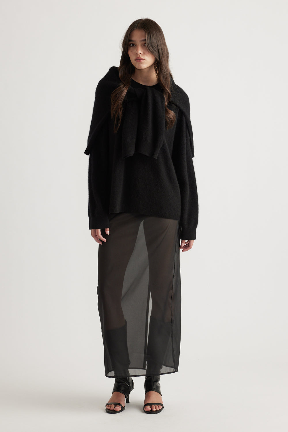 Woman wearing a cozy oversized black wool knit paired with a sheer black maxi skirt and open-toe sandals