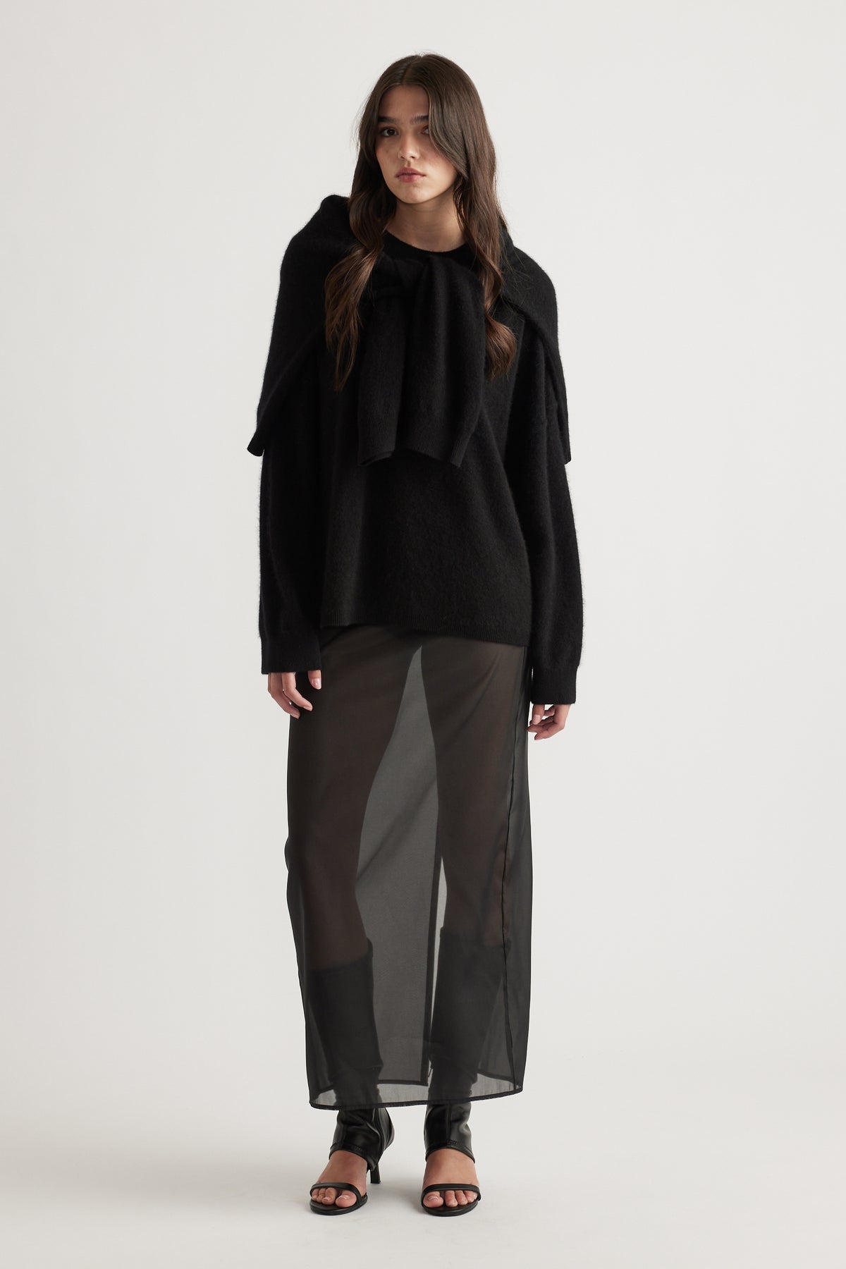 Woman wearing a cozy oversized black wool knit paired with a sheer black maxi skirt and open-toe sandals