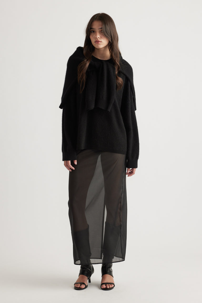 Woman wearing a cozy oversized black wool knit paired with a sheer black maxi skirt and open-toe sandals