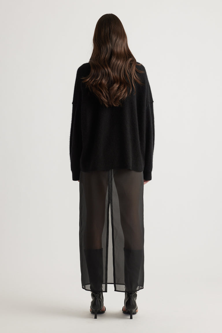Back view of woman wearing a black oversized knit paired with sheer black wide-leg pants and heeled boots