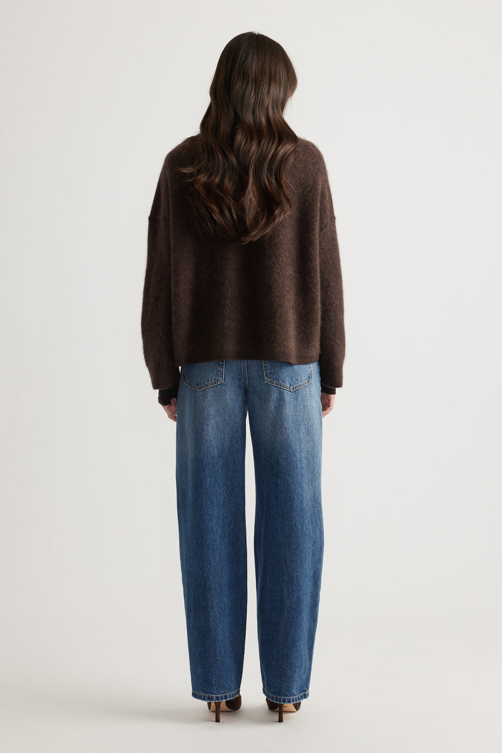 Back view of woman wearing a cozy oversized brown wool knit paired with relaxed blue wide-leg jeans and heels