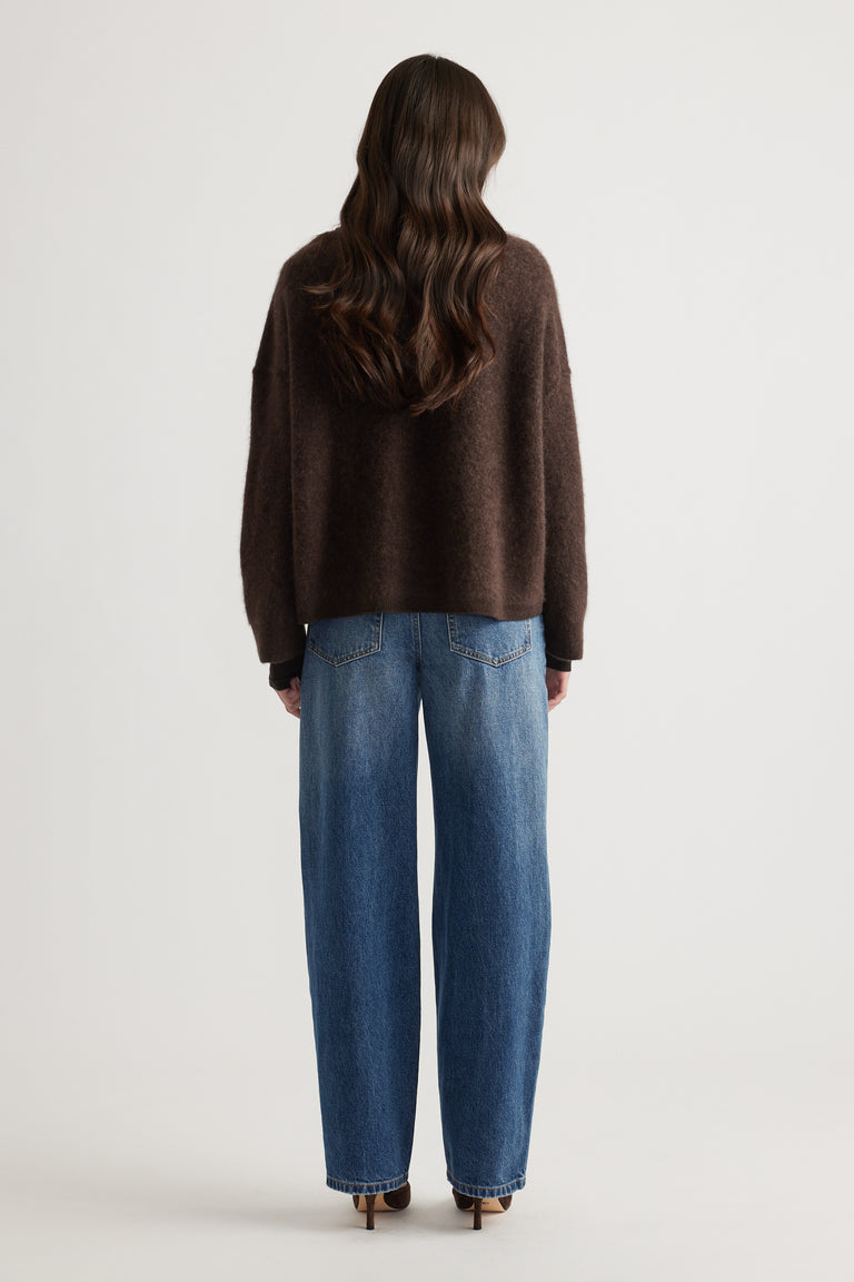 Back view of woman wearing a cozy oversized brown wool knit paired with relaxed blue wide-leg jeans and heels