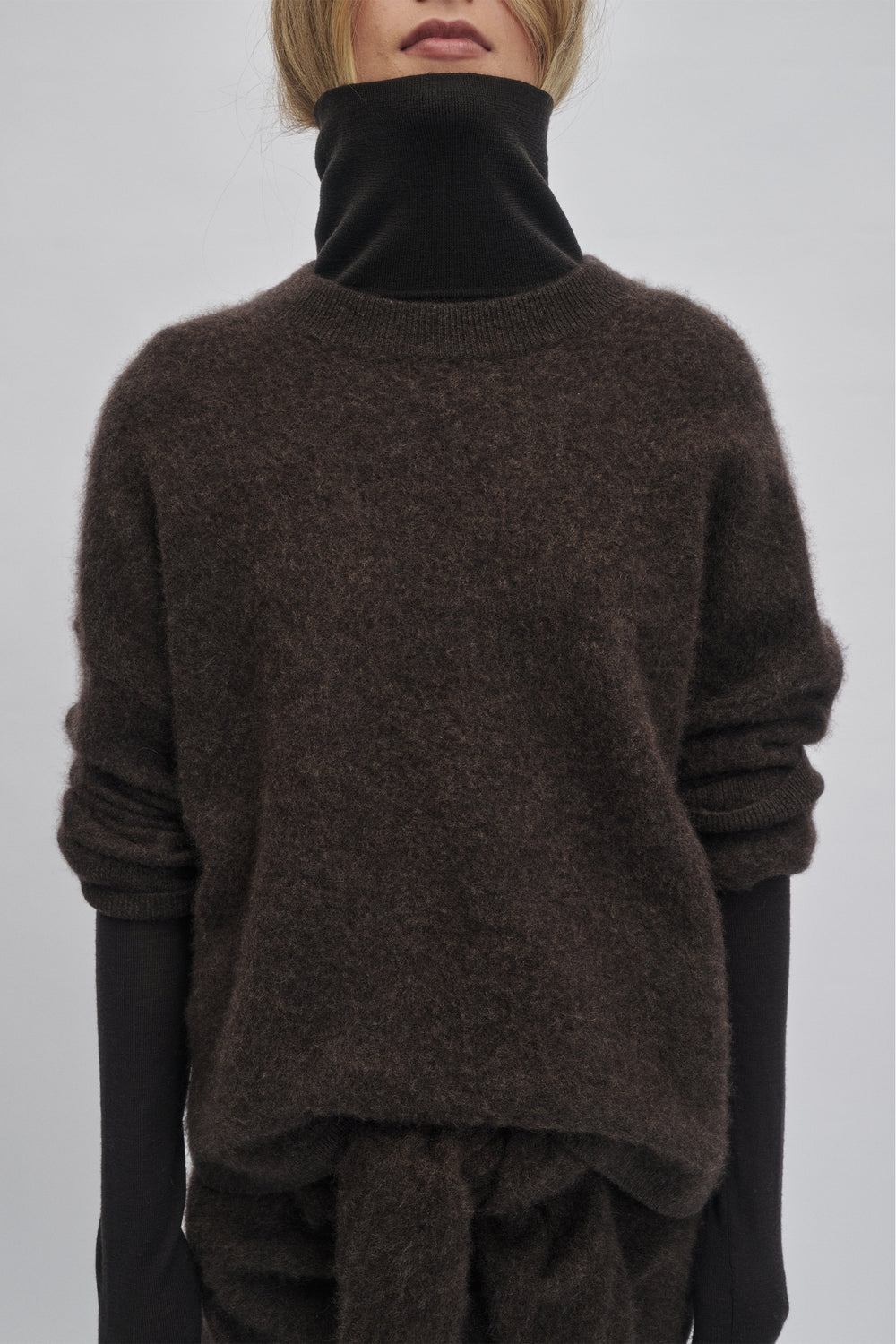 Cozy oversized knit sweater in rich chocolate hue layered over a black long-sleeve top for relaxed warmth and style.