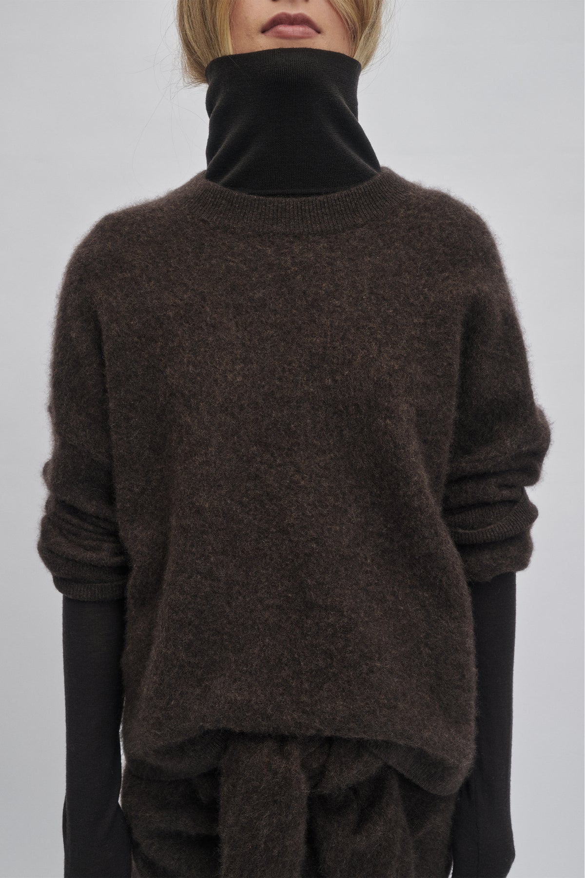 Cozy oversized knit sweater in rich chocolate hue layered over a black long-sleeve top for relaxed warmth and style.