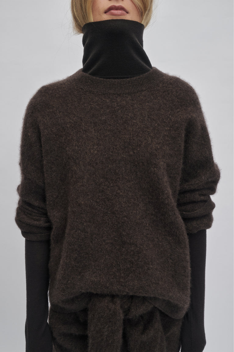 Cozy oversized knit sweater in rich chocolate hue layered over a black long-sleeve top for relaxed warmth and style.