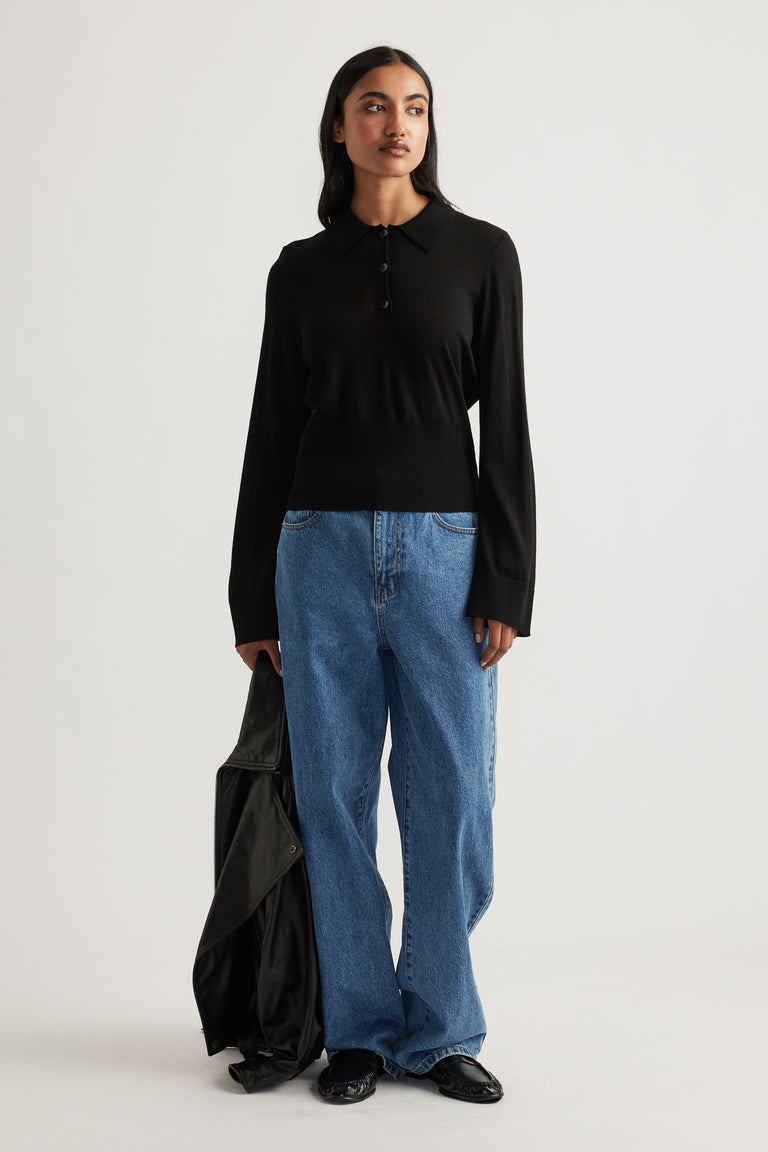 Woman wearing a black fine wool knit polo paired with relaxed blue jeans and holding a black jacket for an effortless look