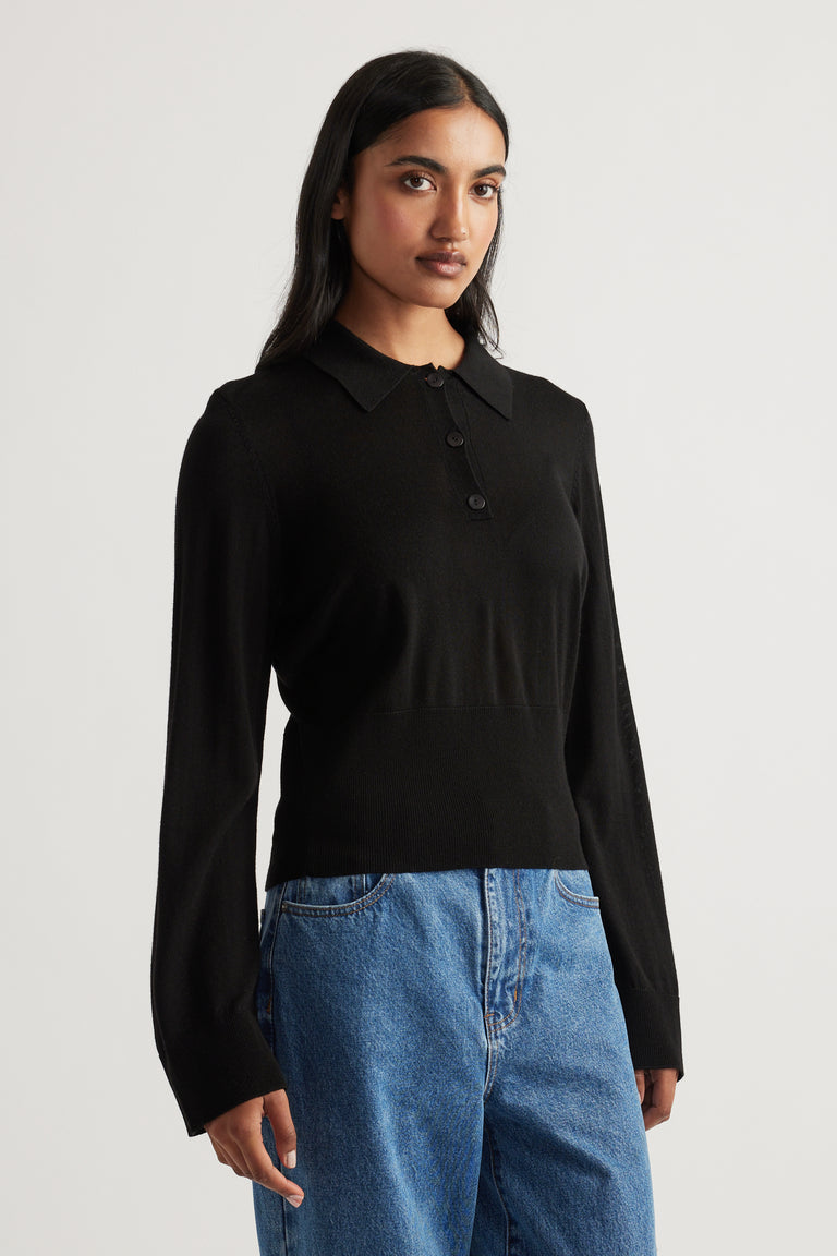 Woman wearing a black fine wool knit polo with button placket paired with relaxed fit blue denim jeans
