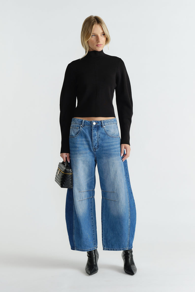 Woman wearing a black high neck jumper paired with relaxed wide-leg blue jeans and black ankle boots