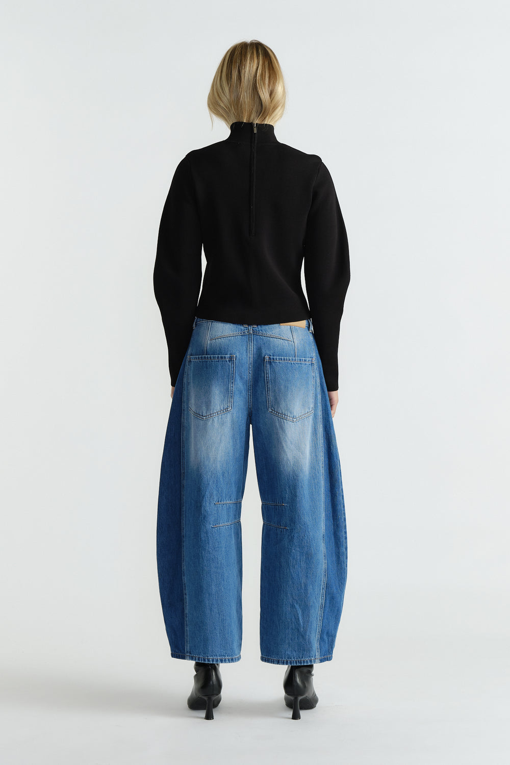 Back view of woman wearing a fitted black high neck jumper paired with wide-leg faded blue jeans and black ankle boots.