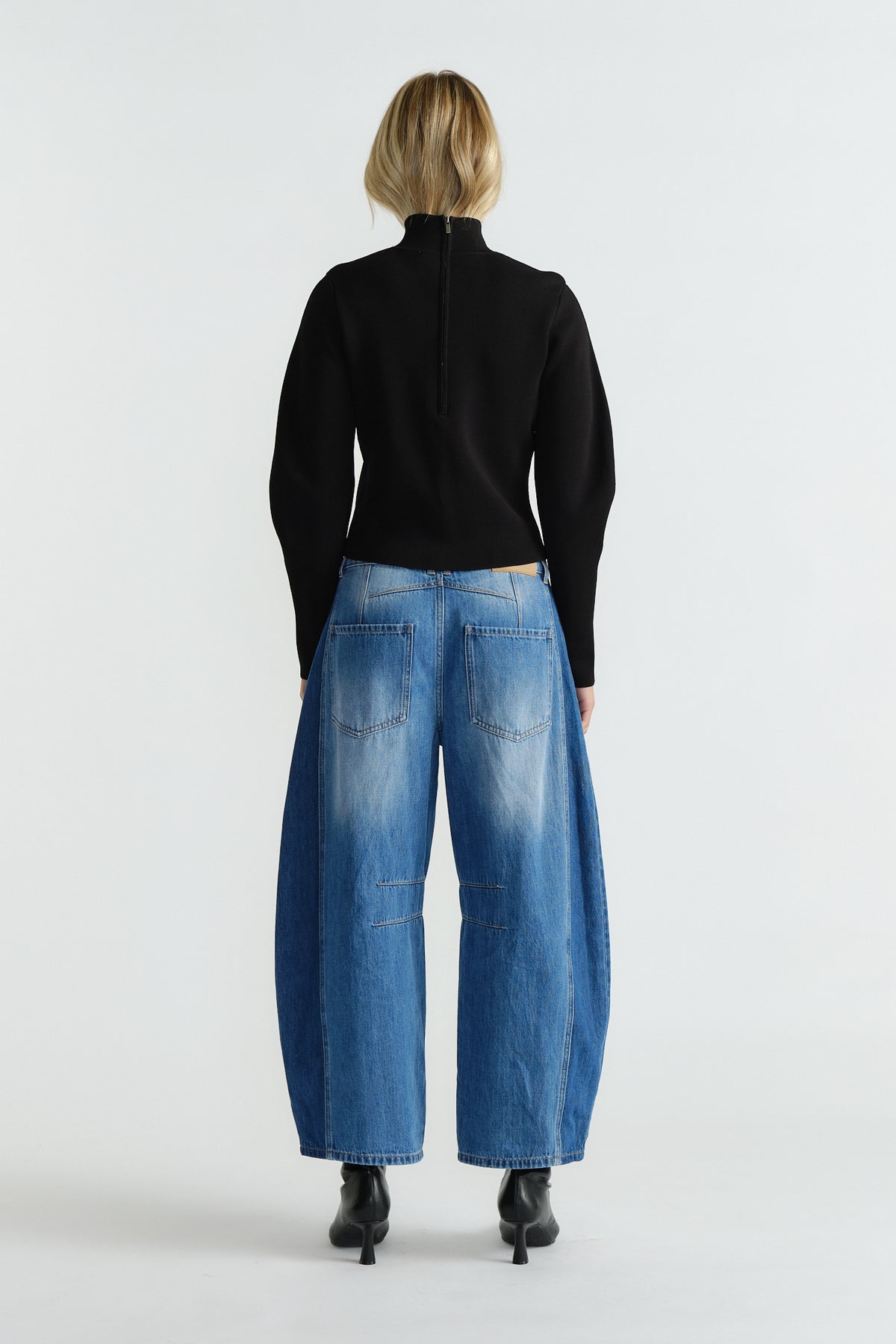 Back view of woman wearing a fitted black high neck jumper paired with wide-leg faded blue jeans and black ankle boots.