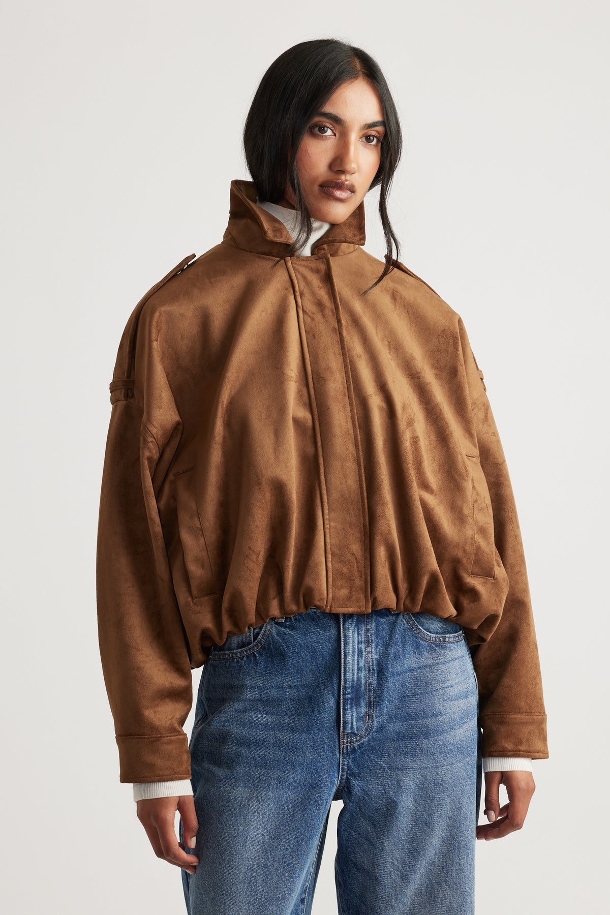 Front view of a loose fit caramel faux suede jacket with high collar, paired with classic blue jeans