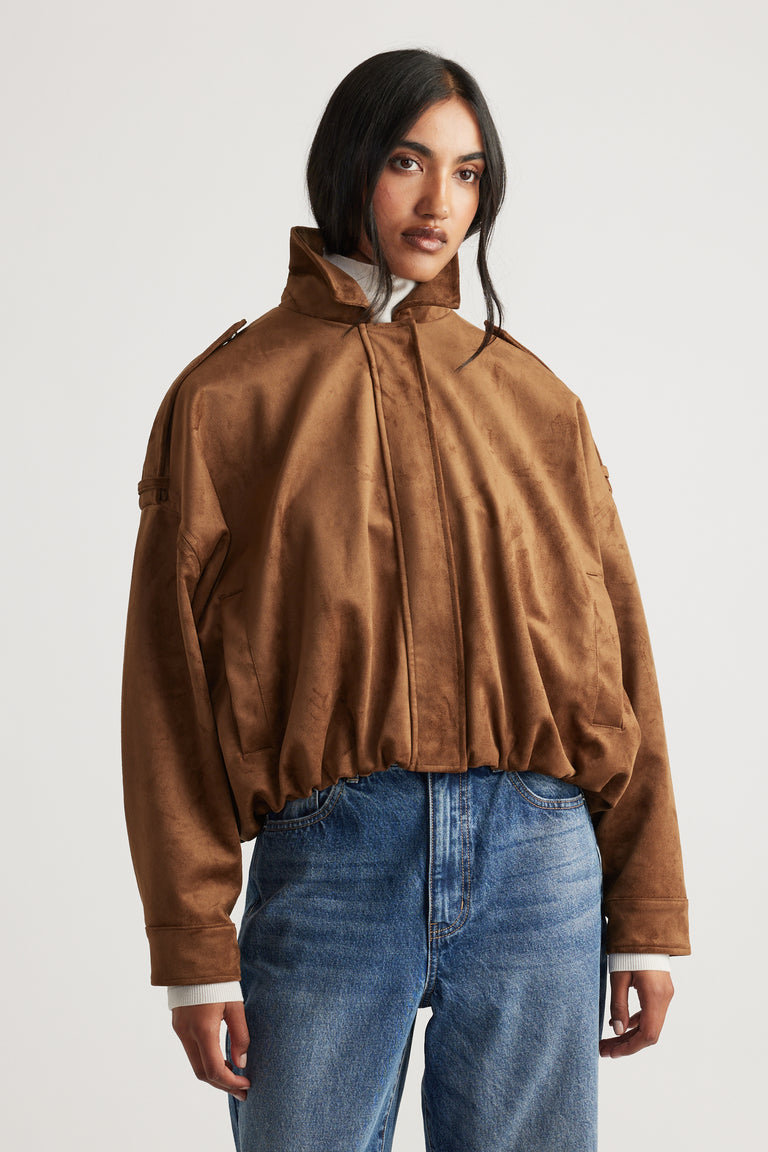 Front view of a loose fit caramel faux suede jacket with high collar, paired with classic blue jeans