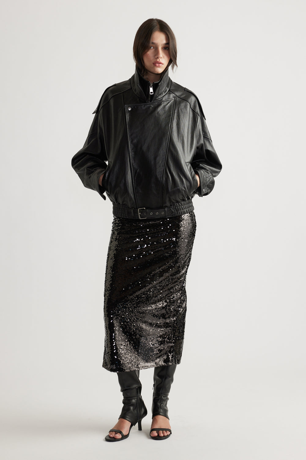 Woman styled in a black leather jacket paired with a shimmering sequin maxi skirt and open-toe heels for edgy glamour