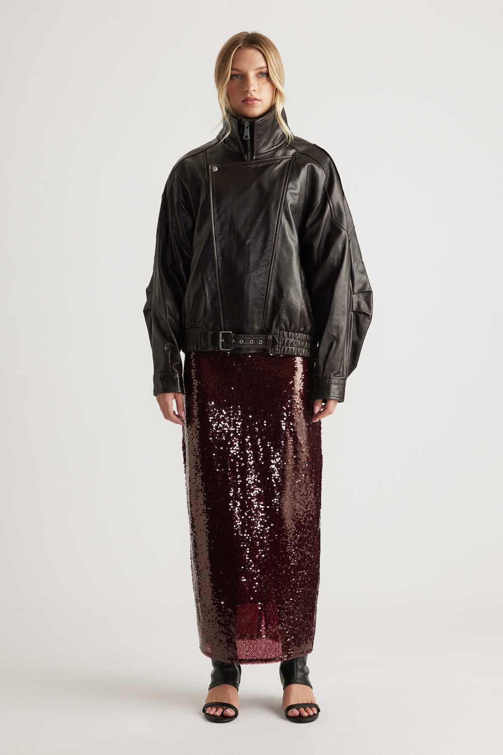 Woman wearing a dark leather jacket styled with a plum sequin maxi skirt and black open-toe heels for a bold look