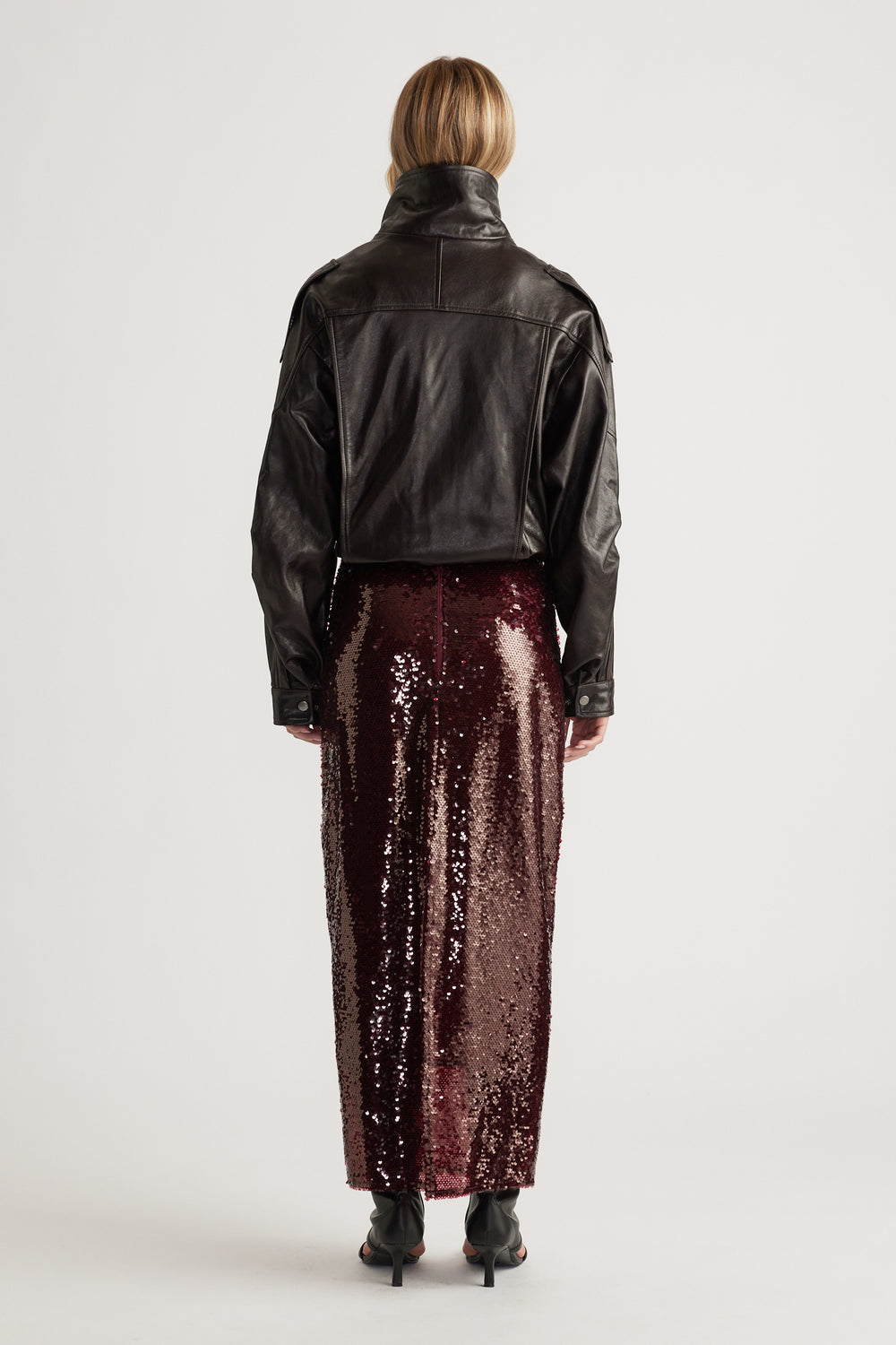Woman wearing a deep plum sequin maxi skirt styled with a cropped black leather jacket and heeled ankle boots