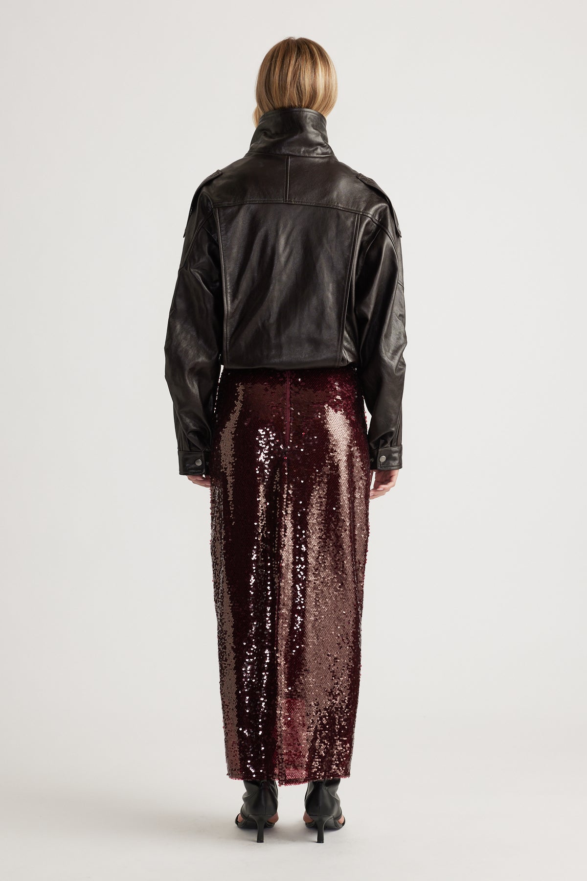 Woman wearing a deep plum sequin maxi skirt styled with a cropped black leather jacket and heeled ankle boots