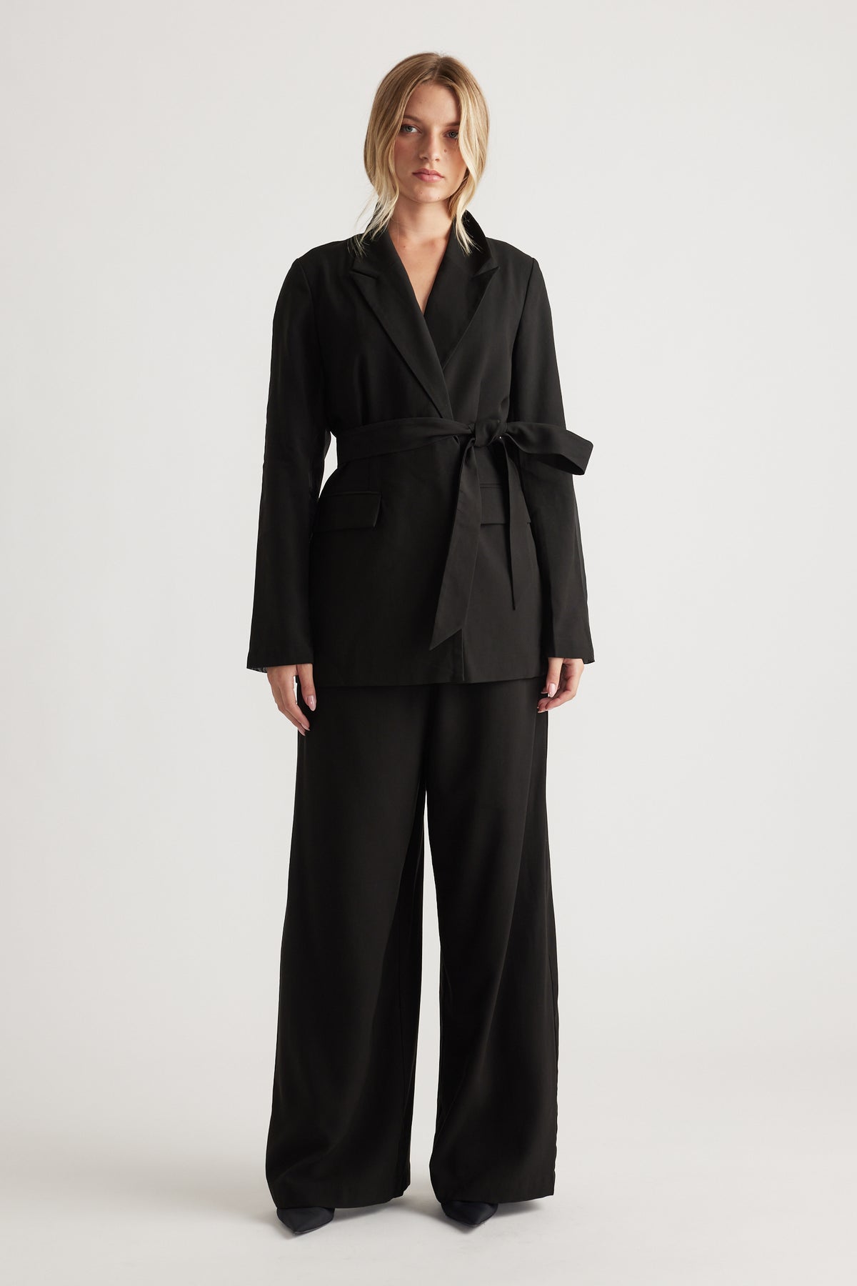 Woman wearing a black belted blazer with wide-leg matching trousers for a sleek, modern tailored look.