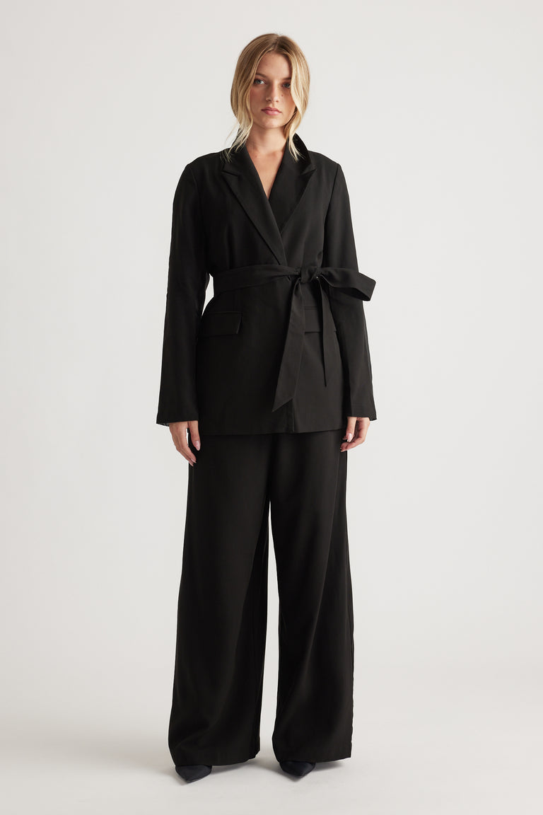 Woman wearing a black belted blazer with wide-leg matching trousers for a sleek, modern tailored look.