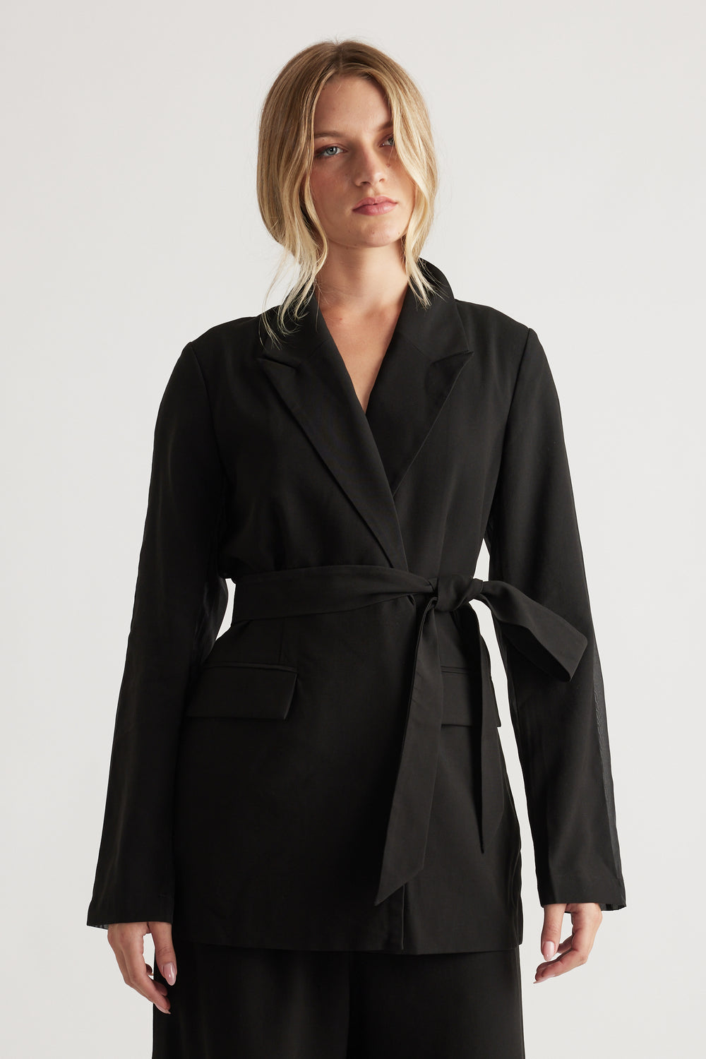 Woman wearing a black belted blazer with notch lapels and flap pockets for a polished, modern look.