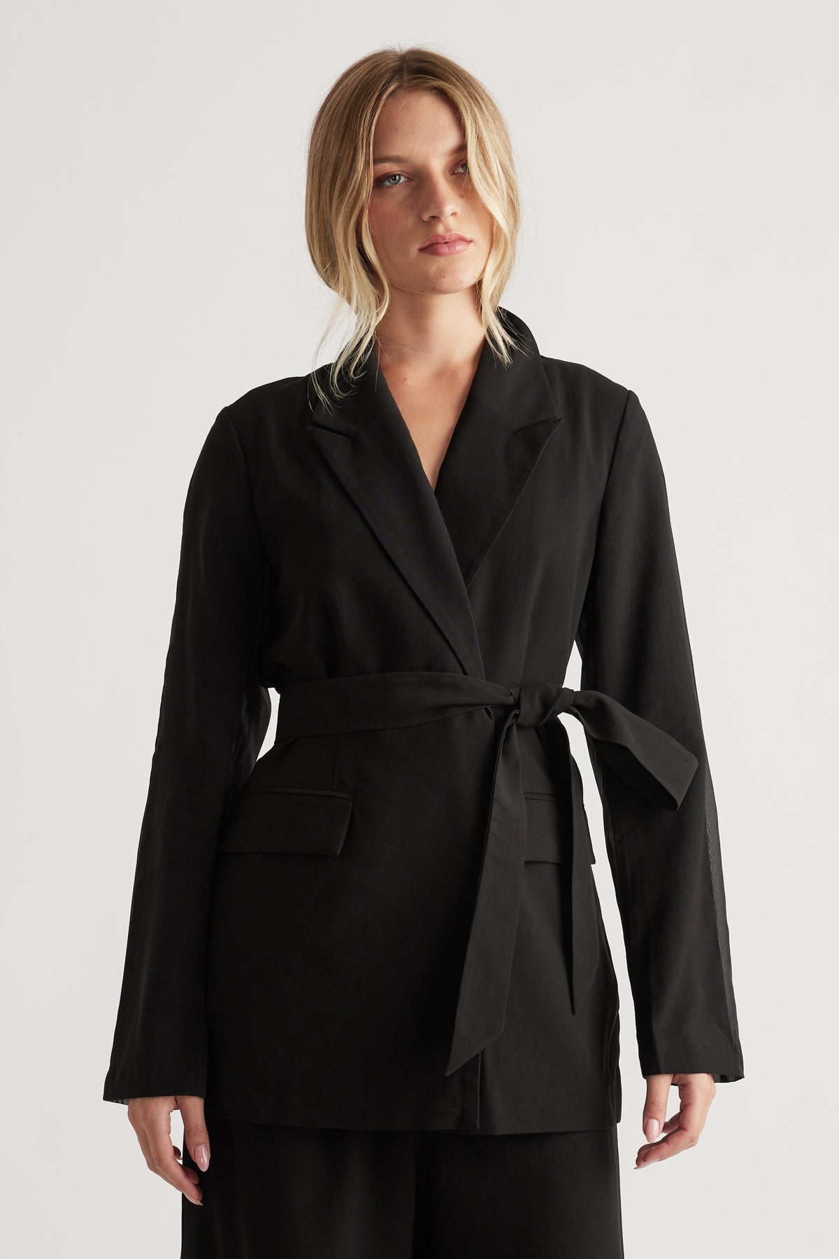 Woman wearing a black belted blazer with notch lapels and flap pockets for a polished, modern look.