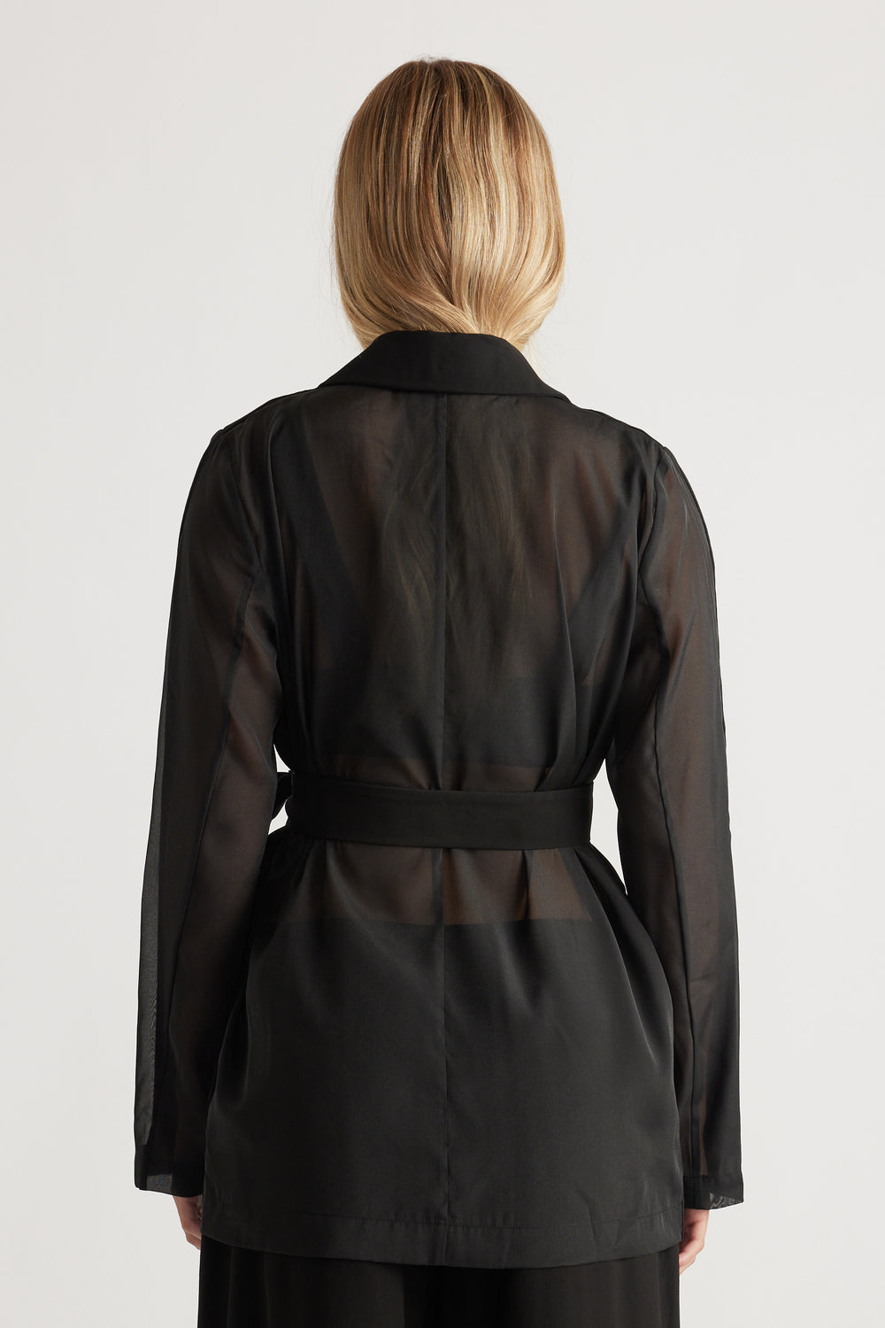 Back view of a woman wearing a sheer black blazer with a structured collar and fitted waist belt
