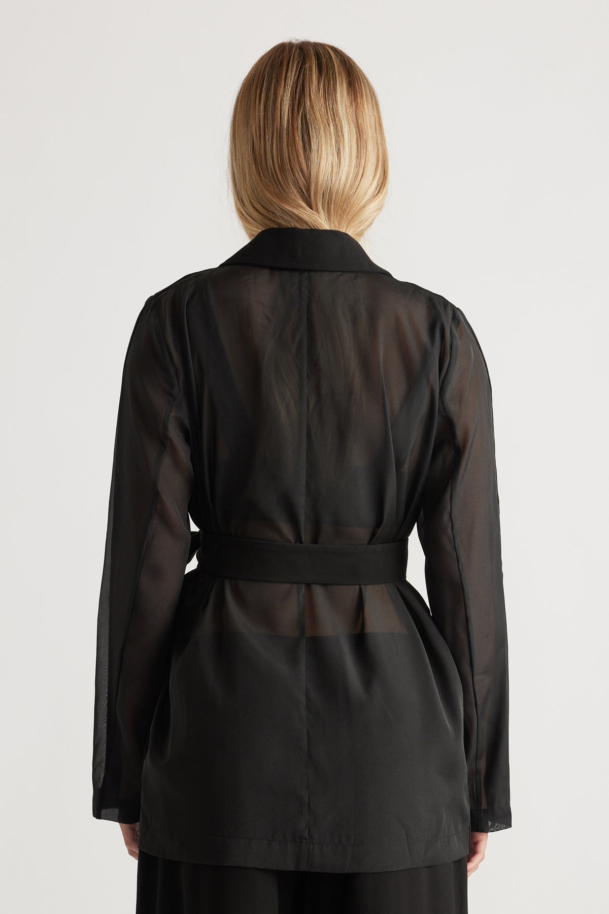 Back view of a woman wearing a sheer black blazer with a structured collar and fitted waist belt