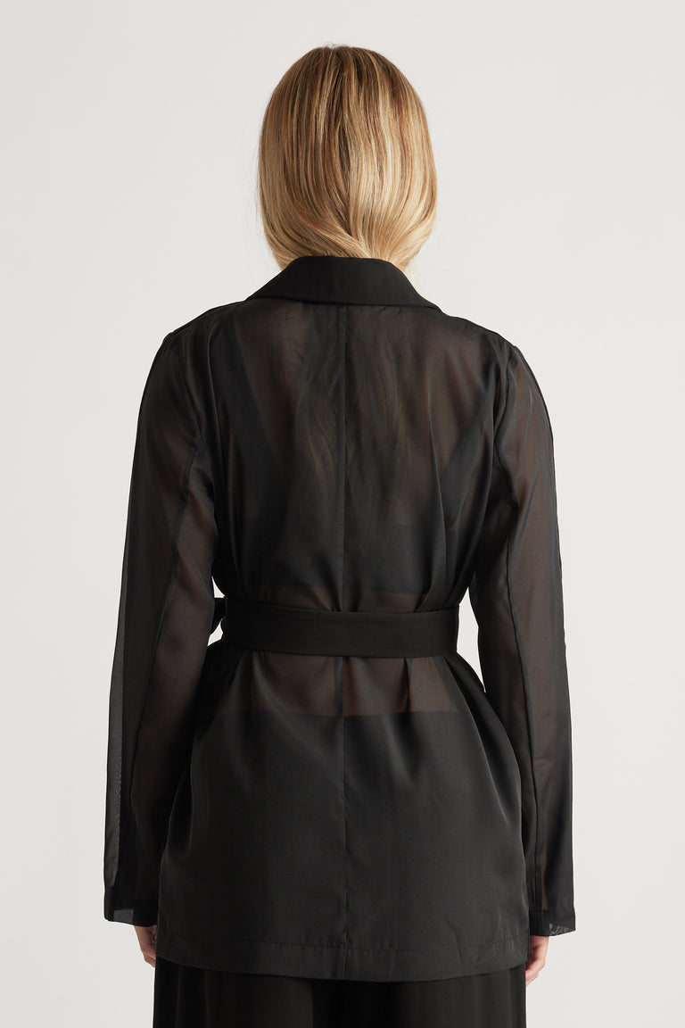 Back view of a woman wearing a sheer black blazer with a structured collar and fitted waist belt