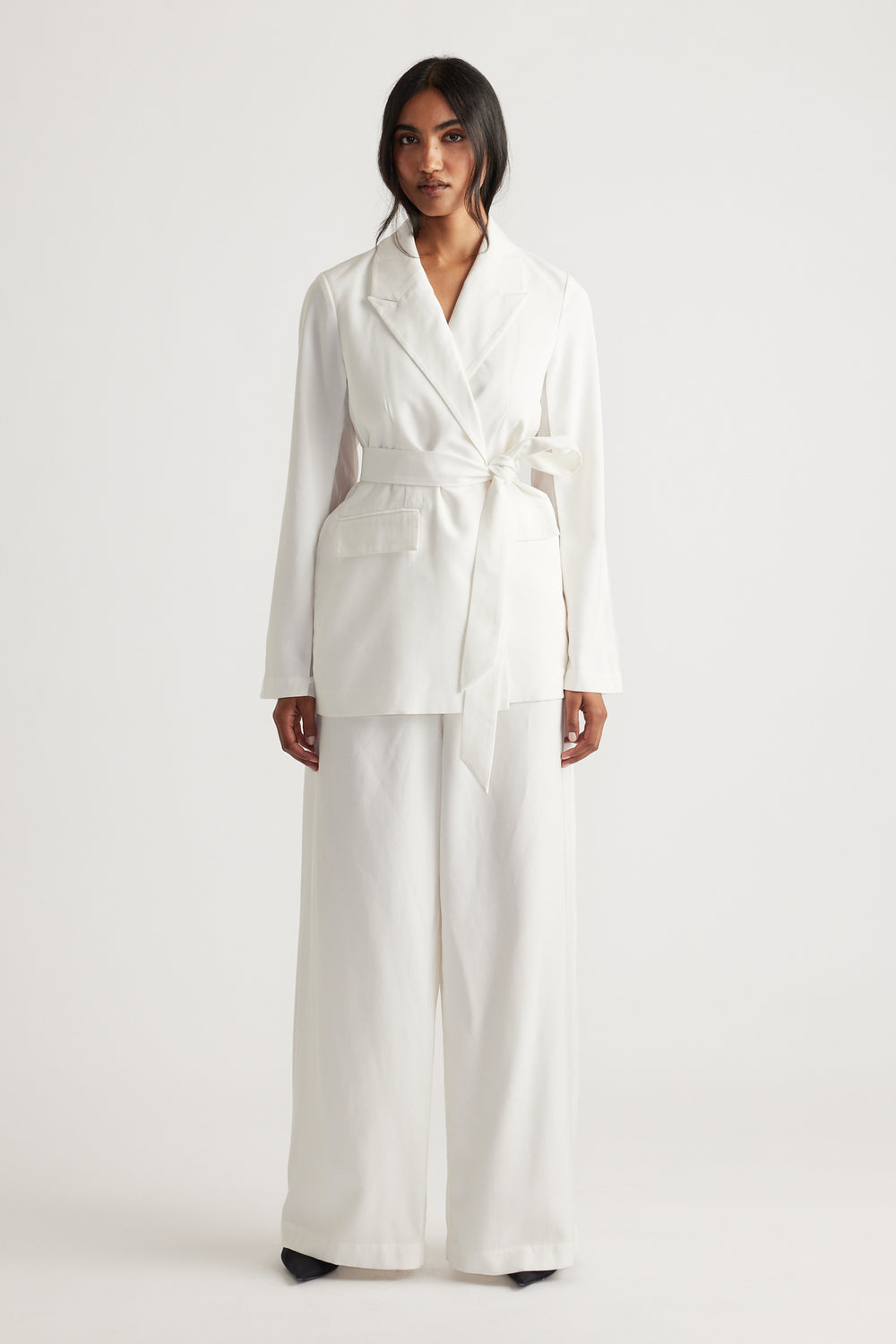 Woman wearing an ivory blazer with a tied waist belt and wide-leg matching pants for a chic, modern look.