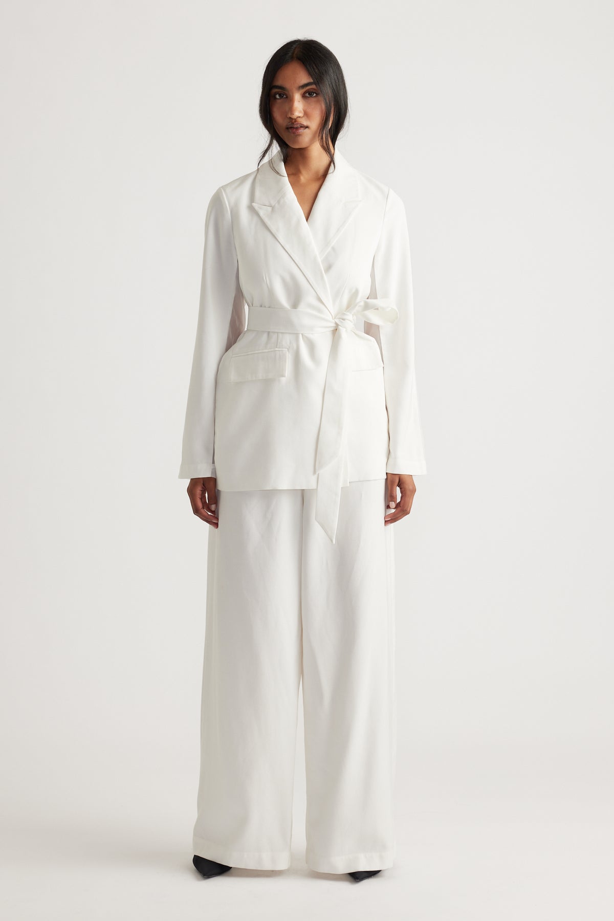 Woman wearing an ivory blazer with a tied waist belt and wide-leg matching pants for a chic, modern look.