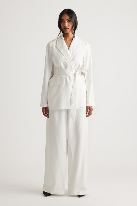 Woman wearing an ivory blazer with a tied waist belt and wide-leg matching pants for a chic, modern look.