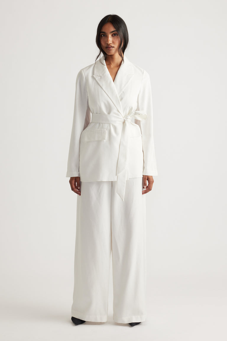 Woman wearing an ivory blazer with a tied waist belt and wide-leg matching pants for a chic, modern look.