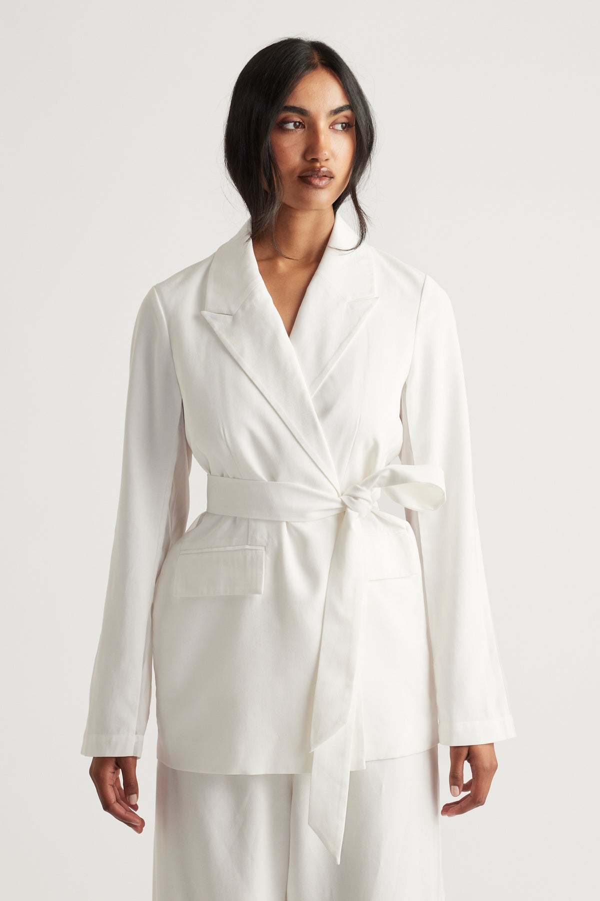 Woman wearing a tailored ivory blazer with a self-tie belt and notch lapel for a sleek, polished look