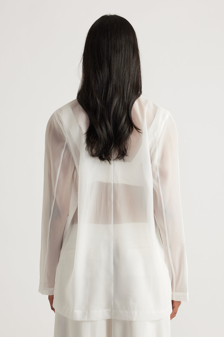 Back view of a lightweight ivory organza blazer with a relaxed fit and long sleeves layered over a white top and pants