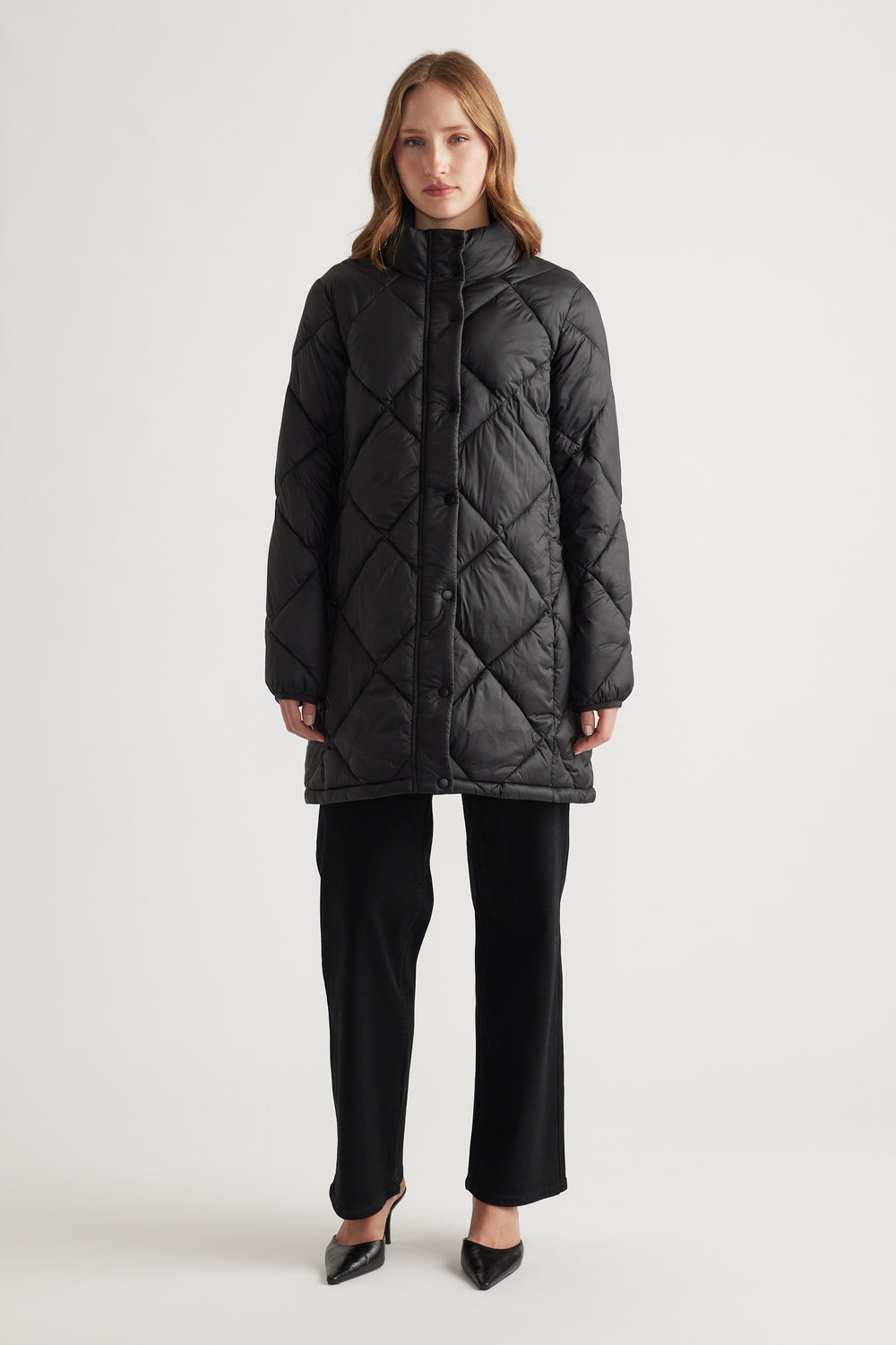 Front view of a woman wearing a black quilted longline puffer jacket paired with black wide-leg pants and black heels