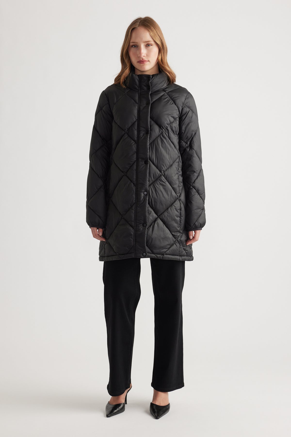 Front view of a woman wearing a black quilted longline puffer jacket paired with black wide-leg pants and black heels