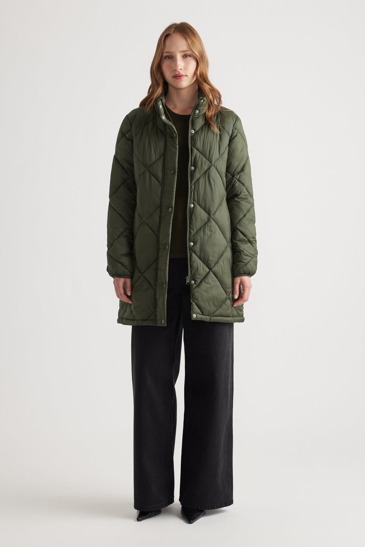Woman wearing an olive green quilted longline jacket paired with wide-leg black pants and pointed shoes