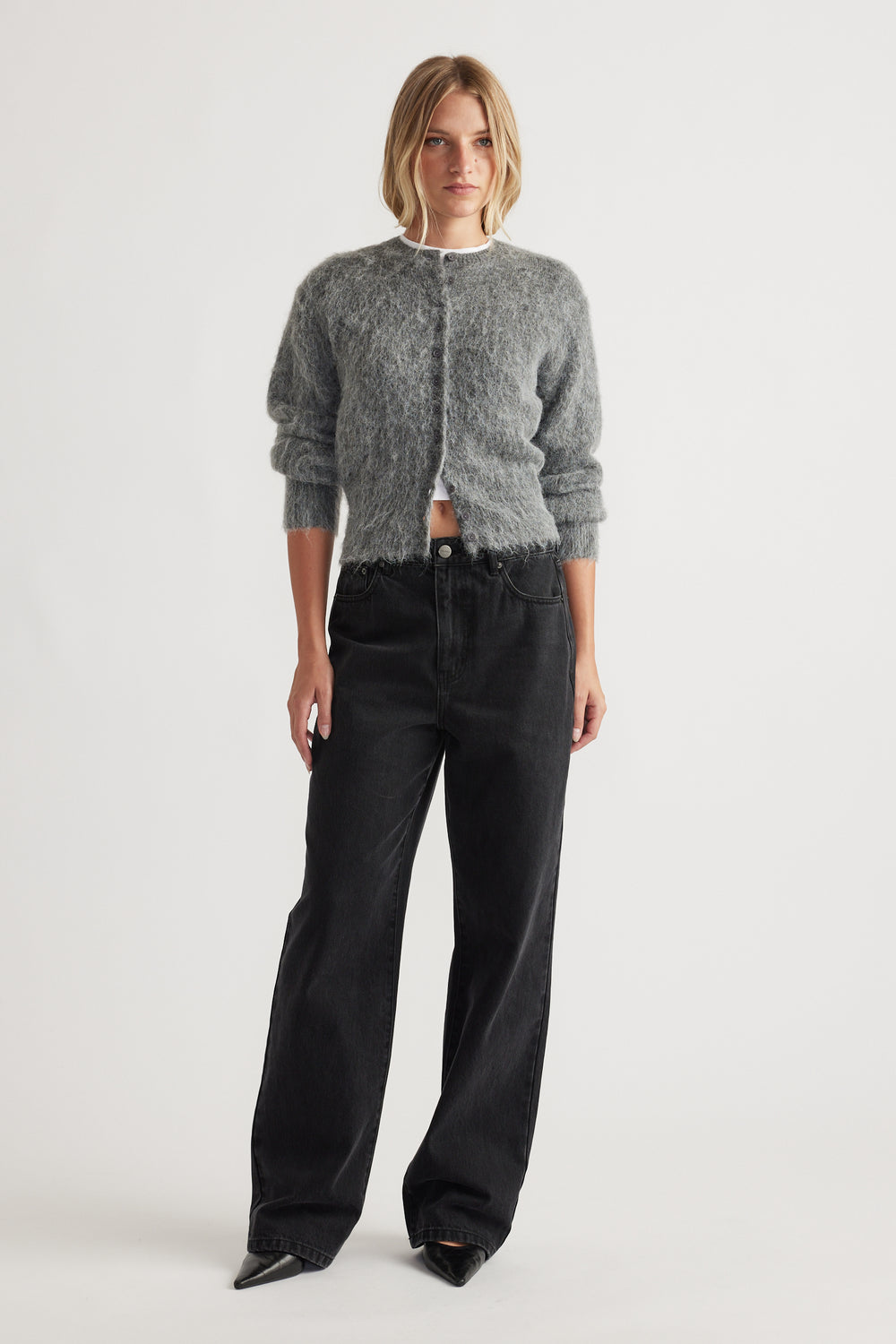 Woman wearing a soft grey fuzzy knit cardigan paired with high-waisted, relaxed black wide-leg jeans and pointed shoes